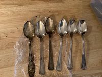 Six sterling silver spoons laid out, three with intact bowls, three with melted spoon bowls, showing varying handle patterns and tarnish.