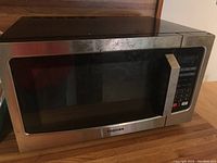 Front view of Toshiba microwave showing the black glass door, stainless steel handle, and keypad with numeric and function buttons on the right.