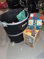 Photo of black Ryobi collapsible bin alongside the Playskool Traveling Pet Hospital original box with toys inside bin partially visible.