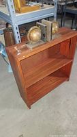 Small wooden two tier bookcase with medium brown finish, two shelves, showing scratches and wear, two vintage-style globe bookends placed on top