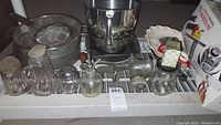 Full lot view showing various kitchenware items including sifters, pitchers, silver stand mixer base, meat grinder, cake pans, mandoline slicer
