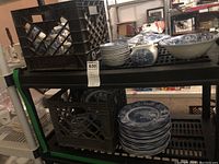 Shelving unit holding multiple crates of plates, bowls and covered pieces in blue and white transferware.