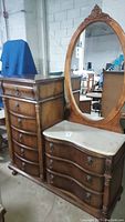 Front side view of wooden marble top vanity dresser with oval mirror, nine drawers with lion head pulls, claw feet, and carved details.