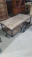 Full view of rustic coffee table with wooden top and bottom shelf and metal frame with wheels