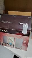 Opened box of TEAC MC-DX20S stereo system showing front with branding and model number, placed on a white surface.
