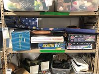 Shelf showing boxed board games Battleship, Blue Thunder, Scene It?, The Game of Greater Providence, baseball bat, ball slinger in box, and Pokémon tapestry folded.