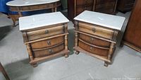 Pair of wooden nightstands with white marble tops and three drawers each. Lion head drawer pulls and claw feet visible.