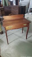 Front view of vintage wooden writing desk showing brass drawer pulls on single drawer and raised back edge.