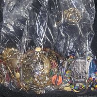 Plastic bag containing assorted mixed costume jewelry with various bracelets and pendants visible