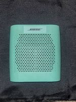 Front view of Bose Bluetooth speaker showing perforated grill and Bose branding, teal colored.