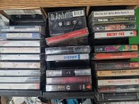 Photo showing the top view of assorted cassette tapes stored in a black plastic case, with visible titles such as The KLF, Britney Fox, Bruce Springsteen, Sheriff, Pat Benatar, and others.