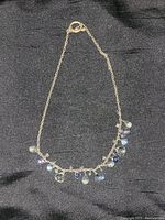 Full view of the gold-tone chain necklace with multiple faceted and dangle multi-colored stones along the necklace length on black fabric background.