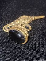 Close-up of bobble fob showing the black stone and detailed gold tone metal.
