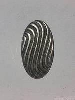 Front view showing oval pendant with flowing linear wave texture in silver-toned metal