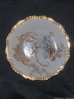 Top view of round Limoges porcelain plate with scalloped gold trim, floral motifs and classical scene