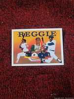 Front view of Reggie Jackson baseball art card showing colorful illustration with three poses and various team caps.