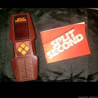 Front view of Split Second handheld game with the screen, yellow directional buttons, and the paper manual titled 'A Race Against Time Split Second'.