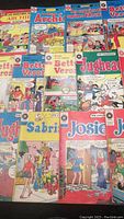Top view showing 13 vintage French Archie comic books arranged in rows. Visible titles include Archie, Betty et Veronica, Jughead, Sabrina, Josie. Covers feature colorful classic comic artwork.