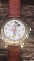 Close-up photo of the vintage Lorus Mickey Mouse watch with brown leather strap and gold-tone case showing Mickey as the watch hands.