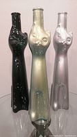 Front view of three cat-shaped wine bottles in black, pearlescent gold, and silver, standing side by side.