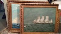 Two framed maritime paintings leaning against a wall, showing both works