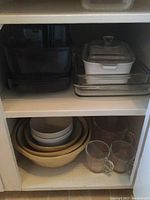 Shelf with black rectangular mixing bowls on the left and two clear glass Corningware rectangular casserole dishes with white ceramic lid on right side.
