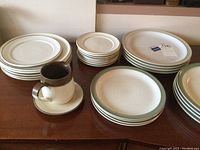 Stacks of various sized plates, cups with saucers, and a pitcher on wooden surface