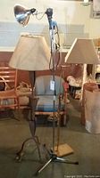 Three vintage metal base floor lamps with varying designs including adjustable arm lamp and clip-on metal shade, situated in a room with chairs and other furniture.
