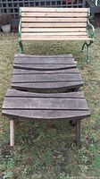 Large wooden garden bench with green cast iron sides and three smaller wooden benches placed in front on grass.