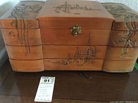 Front view of the jewelry box showing hand carved Asian theme designs on wood and brass clasp.