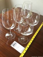 Photo showing all five Riedel glasses on a wooden table with a measuring tape for size reference and a label indicating lot number 203.