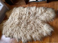 Full view of the cream-colored curly wool sheep skin area rug laid on wooden floor.