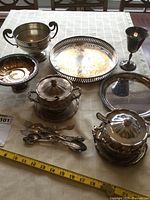 Full view of the lot showing trays, lidded bowls, goblet, footed dish and footed bowl, and serving spoons laid on a tablecloth.