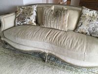 Full view of beige down-stuffed sofa with carved wood frame and three throw pillows