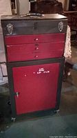 Front view of combined tool chest set showing red and black metal construction with latches and lock area on top chest and rolling bottom cabinet with door.