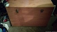 Closed view of natural wood rectangular box with two metal latch clasps in a garage setting.