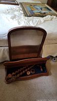 Antique wooden tabletop vanity with a rounded top mirror and disassembled barley twist wooden supports inside the base with blue felt lining, placed on carpet near a bed.