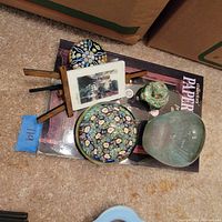 All four glass paperweights, miniature easel with photo, and book on collectible glass paperweights arranged on carpet.
