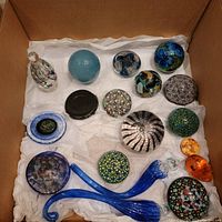 All glass decorative items including paperweights and ornaments arranged on white tissue paper inside a box.