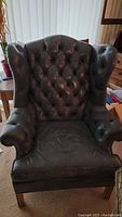 Full front view of the blue leather tufted highback armchair showing winged sides, button tufting, and wooden legs.