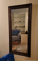 Front view of the large rectangular mirror mounted on a wall, showing the dark brown wooden frame and clear mirror surface reflecting room interior.