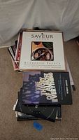 Photo of a stack of cooking and food-related books including Saveur Cooks Authentic French and The Flavour Thesaurus, laid out on a carpeted floor.