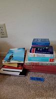 Two stacks of assorted books on carpet against wall, visible titles and colors of book spines.