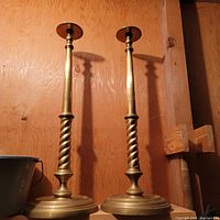 Pair of tall brass candlesticks with twisted stems against wooden background