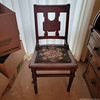 Full front view of vintage wooden Eastlake style chair with carved backrest and floral tapestry seat cushion showing wear.