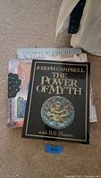 Three books stacked on carpet: top is The Power of Myth by Joseph Campbell with Bill Moyers, bottom two are Thomas McKnight art books.
