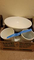 Three white serving bowls in different sizes arranged inside a cardboard box.