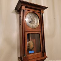 Front view of wooden wall clock showing full case and pendulum window