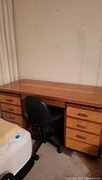Wide front angle photo of the full wooden craftsman style desk showing top surface and drawers with black rolling chair beside it.