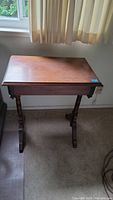 Front view of wood side table under a window showing rectangular top and turned legs.